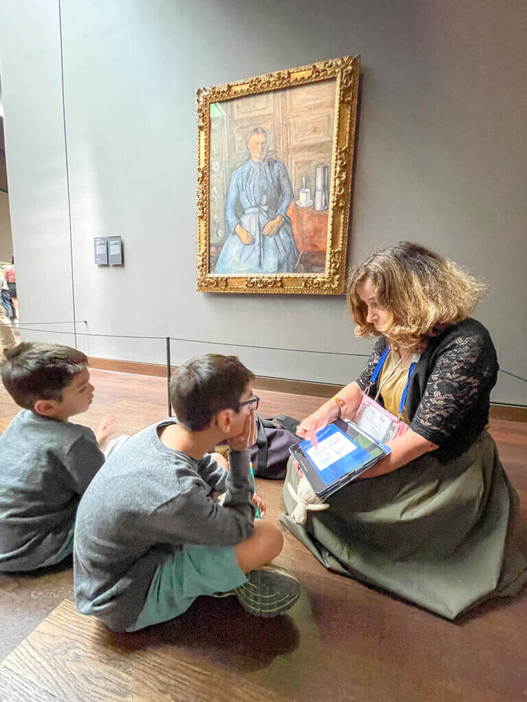 Image of a woman showing two kids an ipad in front of a painting at a Paris museum