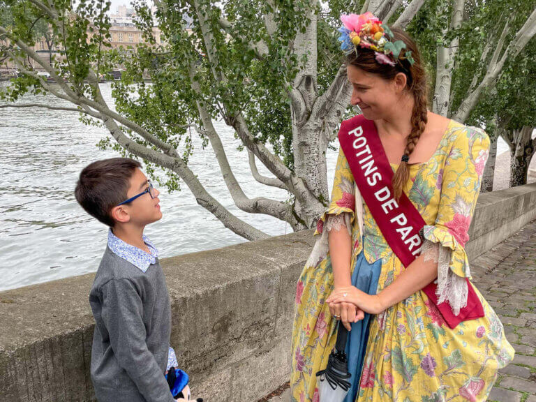 Find out the coolest Paris family tours recommended by top family travel blog Marcie in Mommyland. Imae of a boy chatting with a woman wearing a 1700s costume in Paris