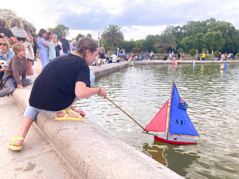 Find out what to do in Paris with teens from a mom who visited Paris with tweens and teens. Image of a girl pushing a toy sailboat at Jardin du Luxembourg in Paris France