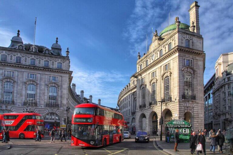 Find out the best travel tips for London by top family travel blog Marcie in Mommyland. Image of some red double-decker buses and tall buildings in London