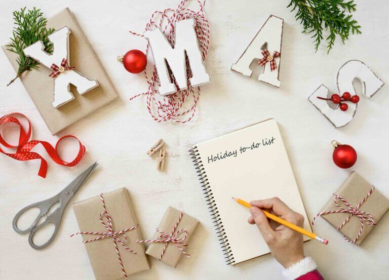 Check out this Christmas Bucket List for families by top family travel blog Marcie in Mommyland. Image of Christmas planning concept, a hand in Santa's dressing is writing a bucket list for winter holidays, view from above