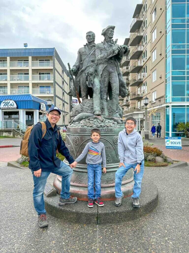 Image of a dad and two boys standing in front of the Lewis and Clark statue in Seaside Oregon