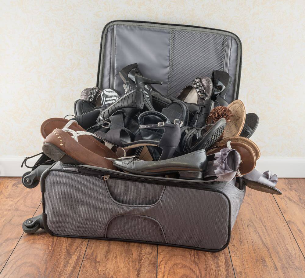 Image of a suitcase overfilled with shoes.