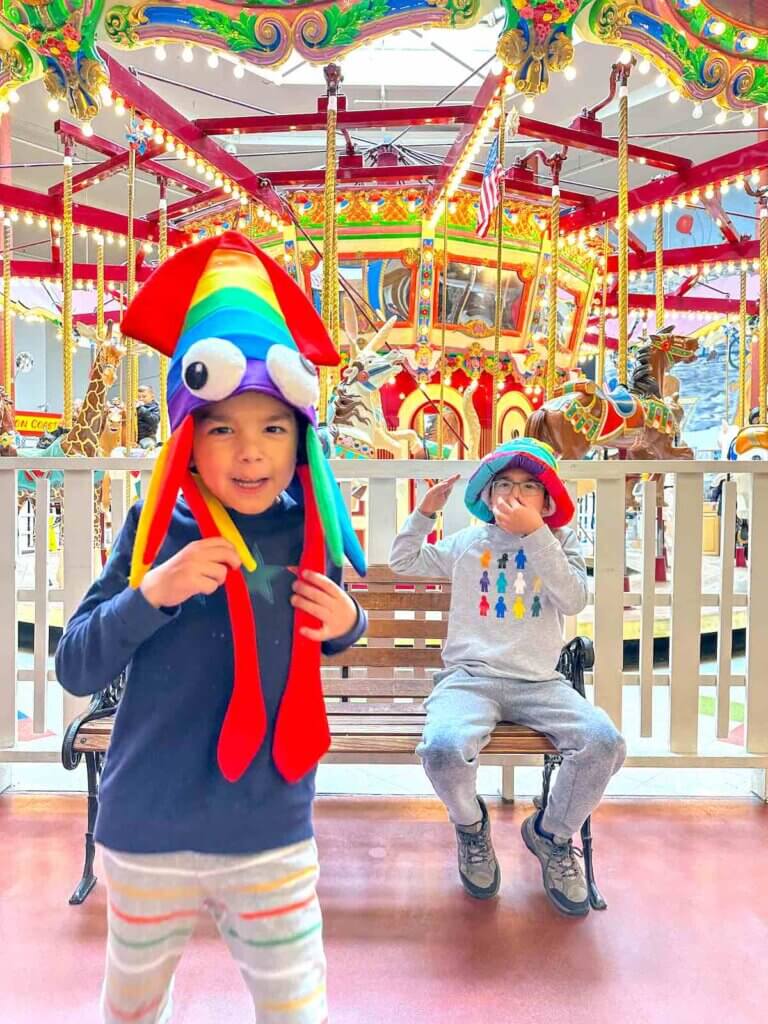 Image of two boys wearing funny rainbow colored hats in front of a carousel in Seaside Oregon