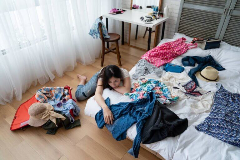 Find out the worse packing mistakes families make, according to top family travel blog Marcie in Mommyland. Image of top view of young asian woman at home packing for luggage in bedroom alone relying thinking daydreaming with head leaning on messy white bed with clothes dresses for vacation. female prepare suitcase