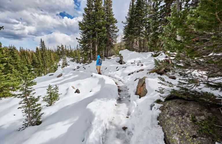 Find out the best places for winter hiking in the USA. Image of Tourist with backpack hiking on snowy trail in Rocky Mountain National Park, Colorado, USA.