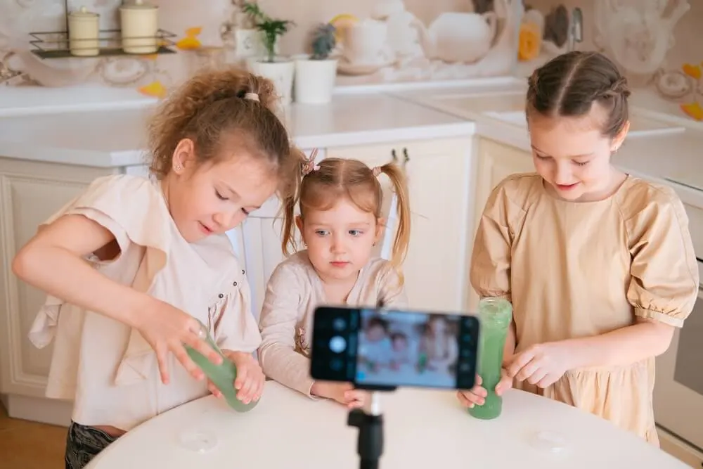 Three cute sisters playing slime on a kitchen and making video content for internet blog