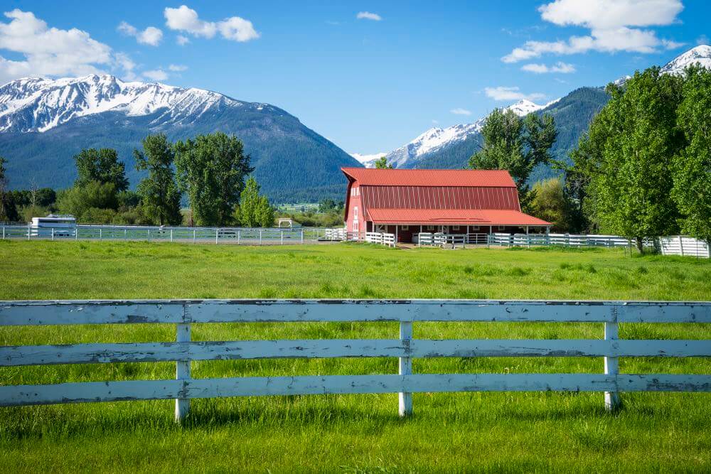 Joseph is one of the cutest Oregon towns. Image of a red barn on a grassy lawn with Wallowa Mountains in the background