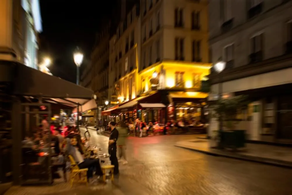 Blurry motion image of people at cafes and bistros at night in Paris.