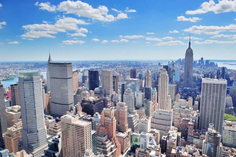 Find out the best New York City hotels for families recommended by top family travel blog Marcie in Mommyland. Image of New York City Manhattan midtown aerial panorama view with skyscrapers and blue sky in the day.