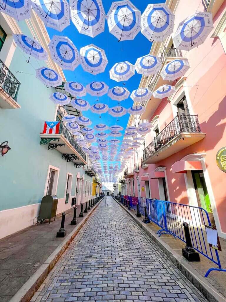 Image of a colorful street with umbrellas in the air.