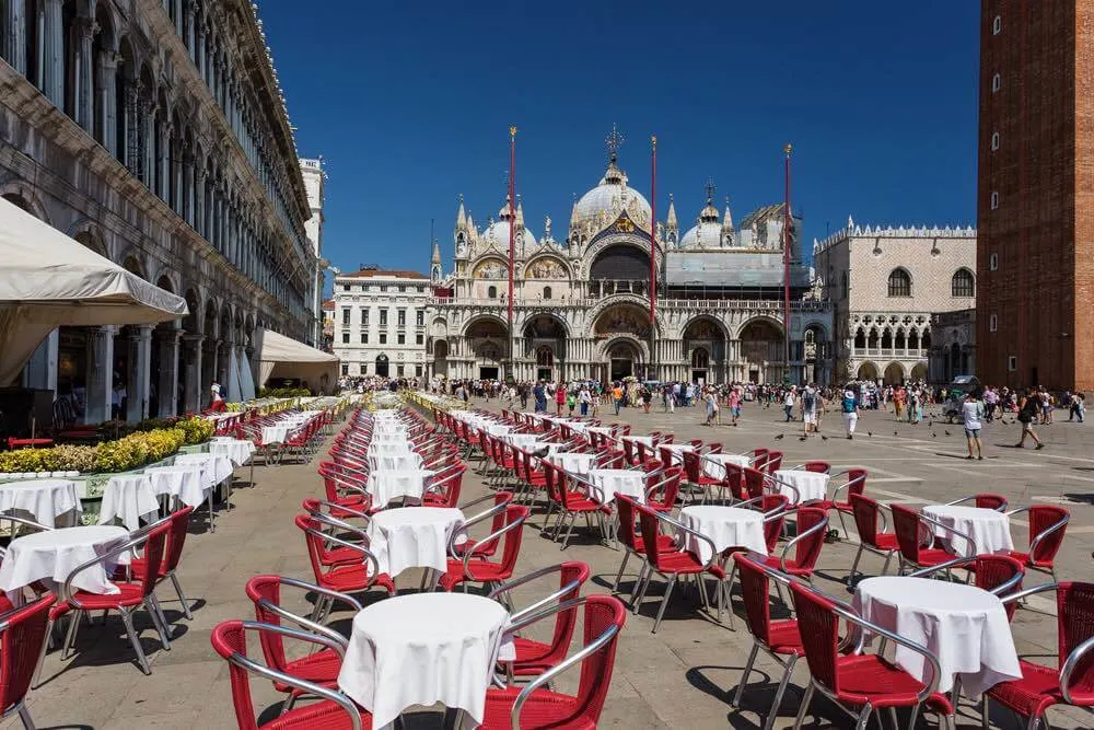 Venice in Italy, Piazza San Marco with the Basilica of Saint Mark. Cafe tables and chairs in foreground