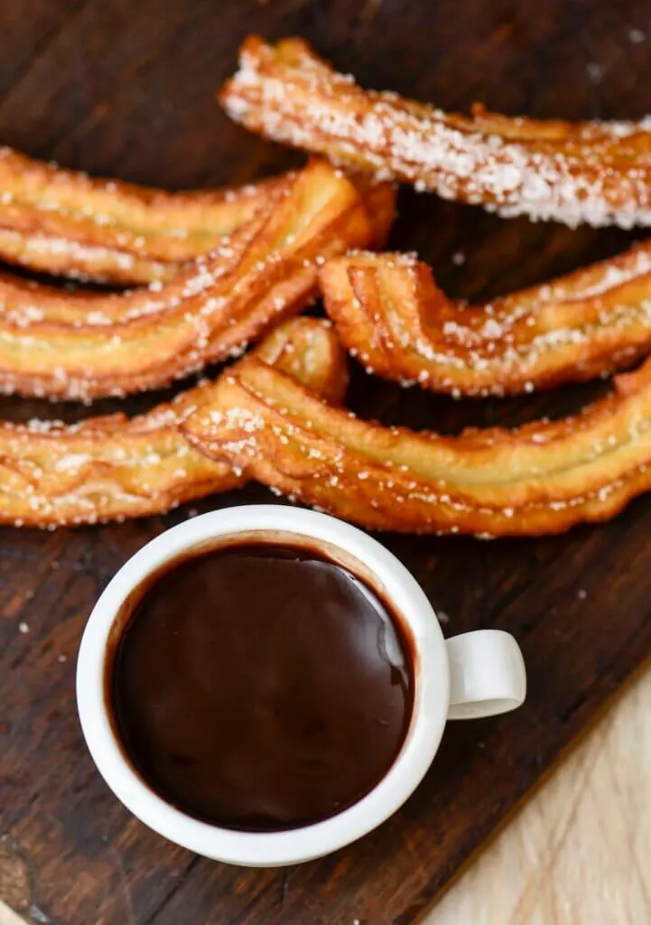 high-angle shot of some churros and a cup of hot chocolate, a typical Spanish sweet snack, on a rustic wooden table
