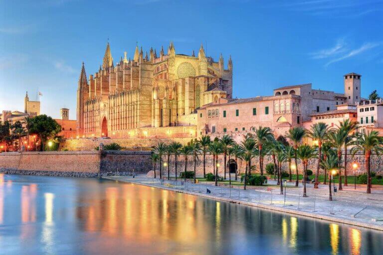 Check out these Mallorca tips for first timers recommended by top family travel blog Marcie in Mommyland. Image of Cathedral of Palma de Majorca reflecting on the water at evening