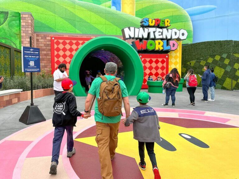 Check out these expert tips for Super Nintendo World Universal Studios Hollywood by top family travel blog Marcie in Mommyland. Image of a dad and two boys walking into Super Nintendo World.