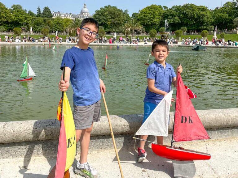 Find out the coolest things to do on a Paris family vacation recommended by top family travel blog Marcie in Mommyland. Image of two boys with toy boats at Luxembourg Gardens in Paris