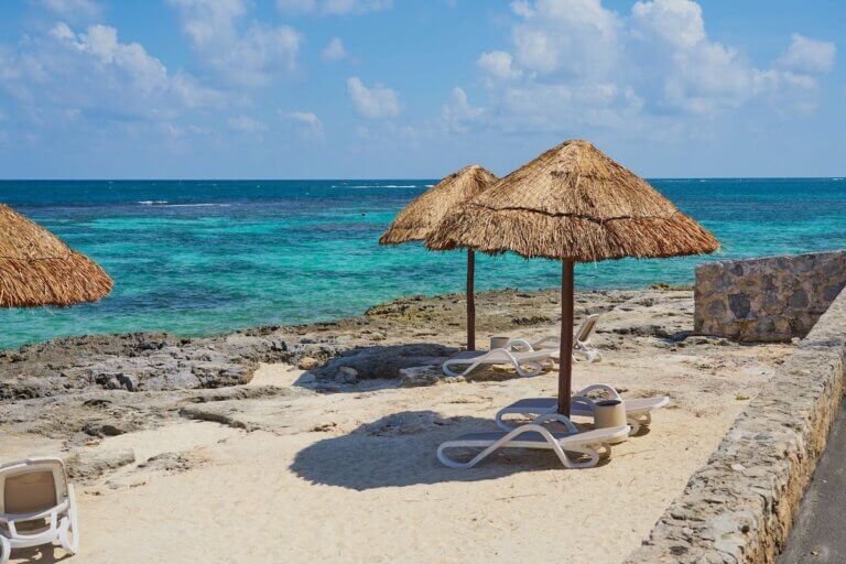 Check out the best all inclusive Cancun resorts for families recommended by top family travel blog Marcie in Mommyland. Image of Beach umbrellas made of straw on the shores of the Caribbean Sea in Mexico