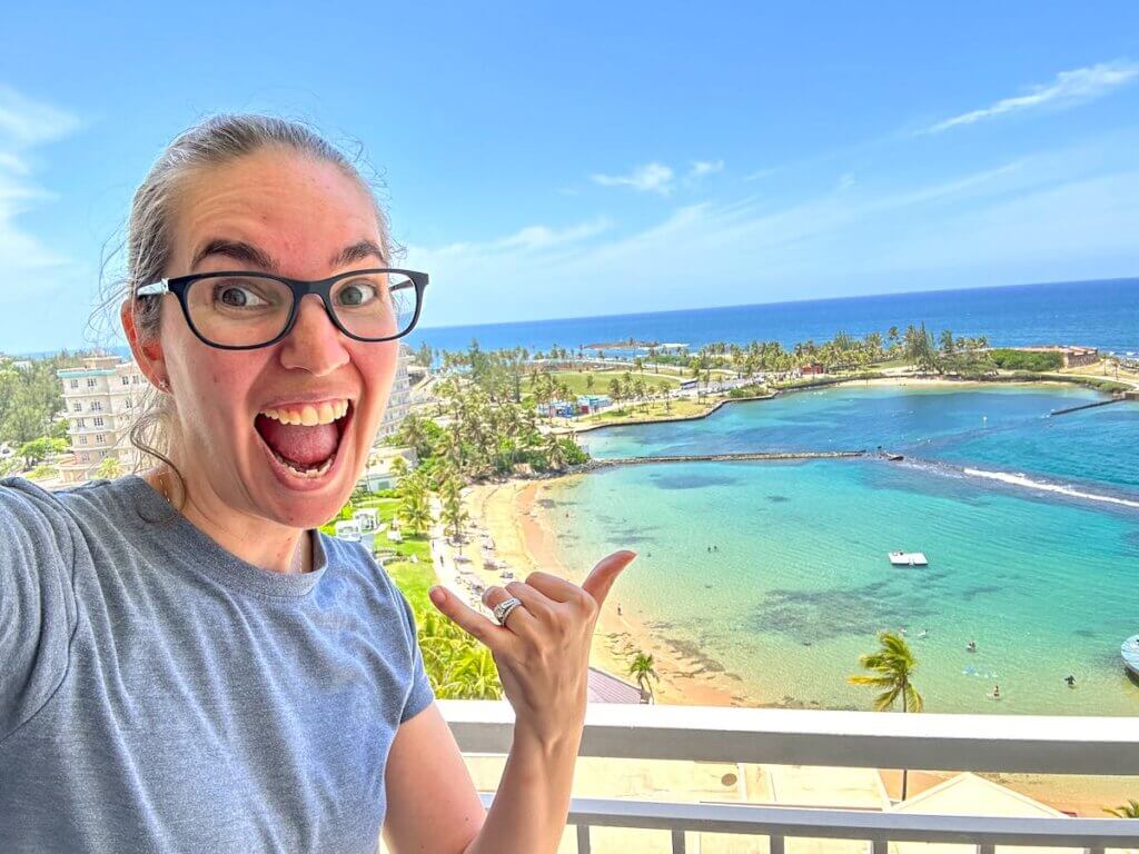 Image of a woman taking a selfie on the deck of her room at the Caribe Hilton overlooking the beach