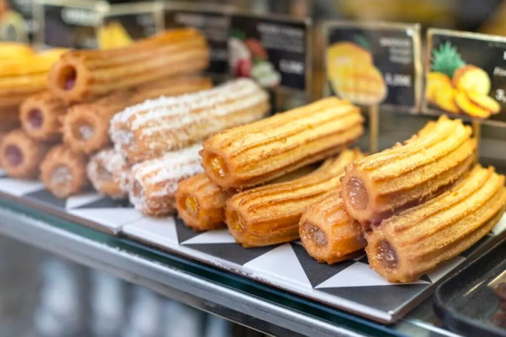 Image of Different types of traditional sweet spanish dessert churros with filling on the market or bakery showcase. Hot baked pastry dish