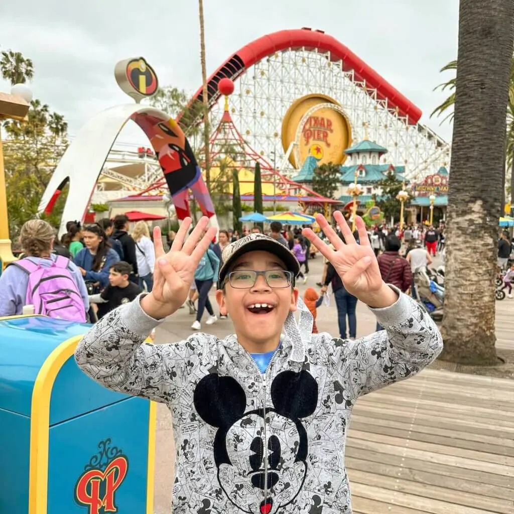Image of a boy holding up 8 fingers in front of the Incredicoaster at Disney California Adventure Park