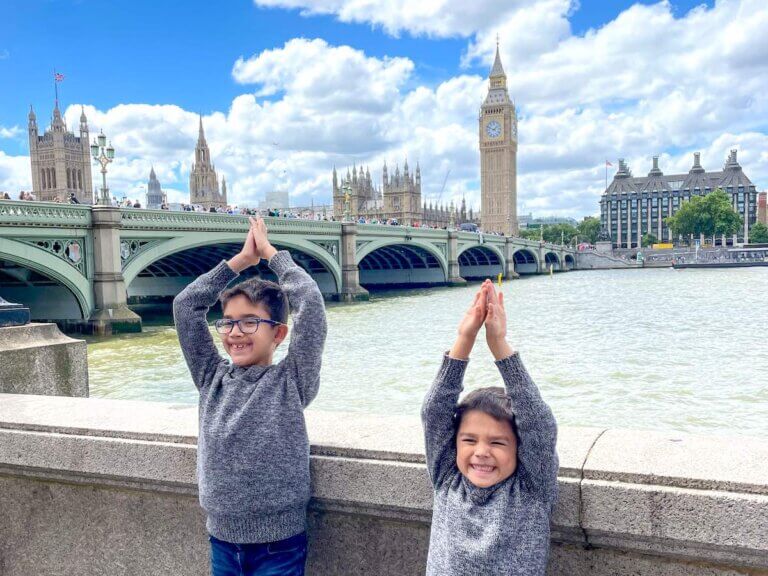 Check out the coolest London things to do for kids recommended by top family travel blog Marcie in Mommyland. Image of two boys pretending to be Big Ben with the actual Big Ben in the background