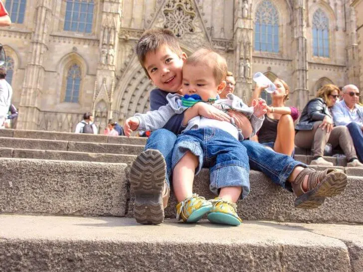 Find out the coolest things to do in Barcelona with kids recommended by top family travel blog Marcie in Mommyland. Image of a baby and a toddler sitting on the steps of Sagrada Familia