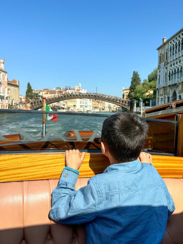 Image of a boy looking out the back of a water taxi in Venice