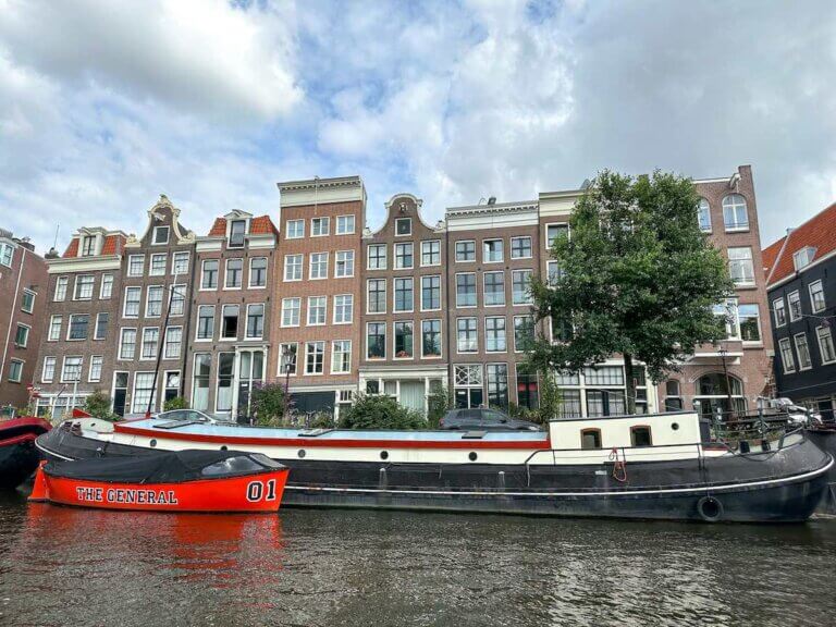 Check out these essential Amsterdam travel tips by top family travel blog Marcie in Mommyland. Image of an Amsterdam canal with boats and buildings