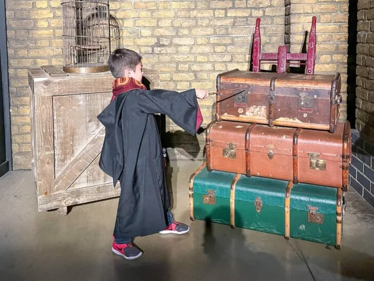 Check out these awesome London tours for families recommended by top family travel blog Marcie in Mommyland. Image of a boy wearing a Hogwarts robe casting a spell on some luggage