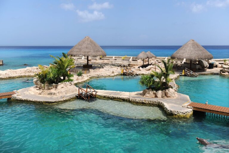 Check out this comparison of Cancun vs Cozumel by top family travel blog Marcie in Mommyland. Image of Dolphinarium in Cozumel Mexico with beach in background