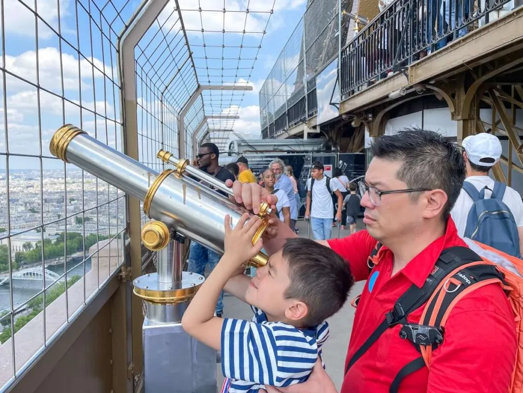 Image of a dad and son looking through a telescope at the summit of the Eiffel Tower in Paris.