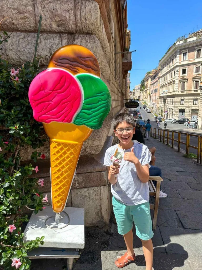 Image of a boy holding gelato in front of an oversized ice cream cone in Rome