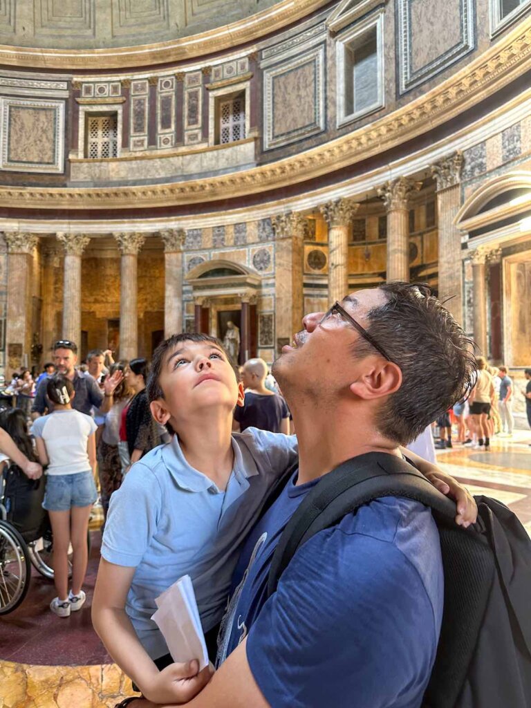 Image of a dad holding a boy as they look up at the ceiling of the Pantheon in Rome Italy