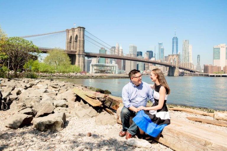 Check out these amazing New York City travel tips recommended by top travel blog Marcie in Mommyland. Image of a couple sitting on log in front of a bridge in NYC
