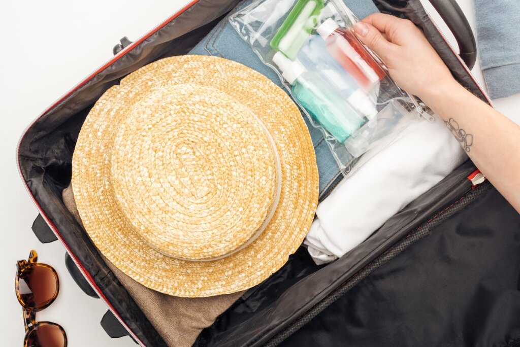 Image of a suitcase with a straw hat, toiletries, and sunglasses