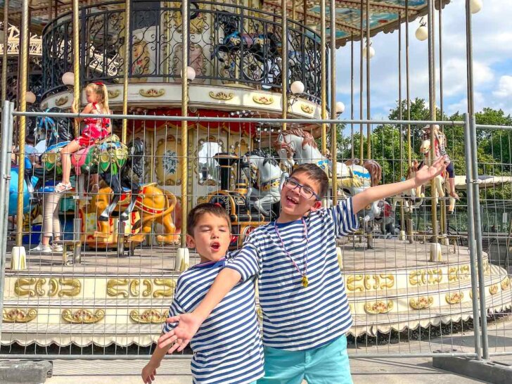 Check out the best tips for visiting Paris with kids recommended by top family travel blog Marcie in Mommyland. Image of two boys in front of a carousel in Paris France