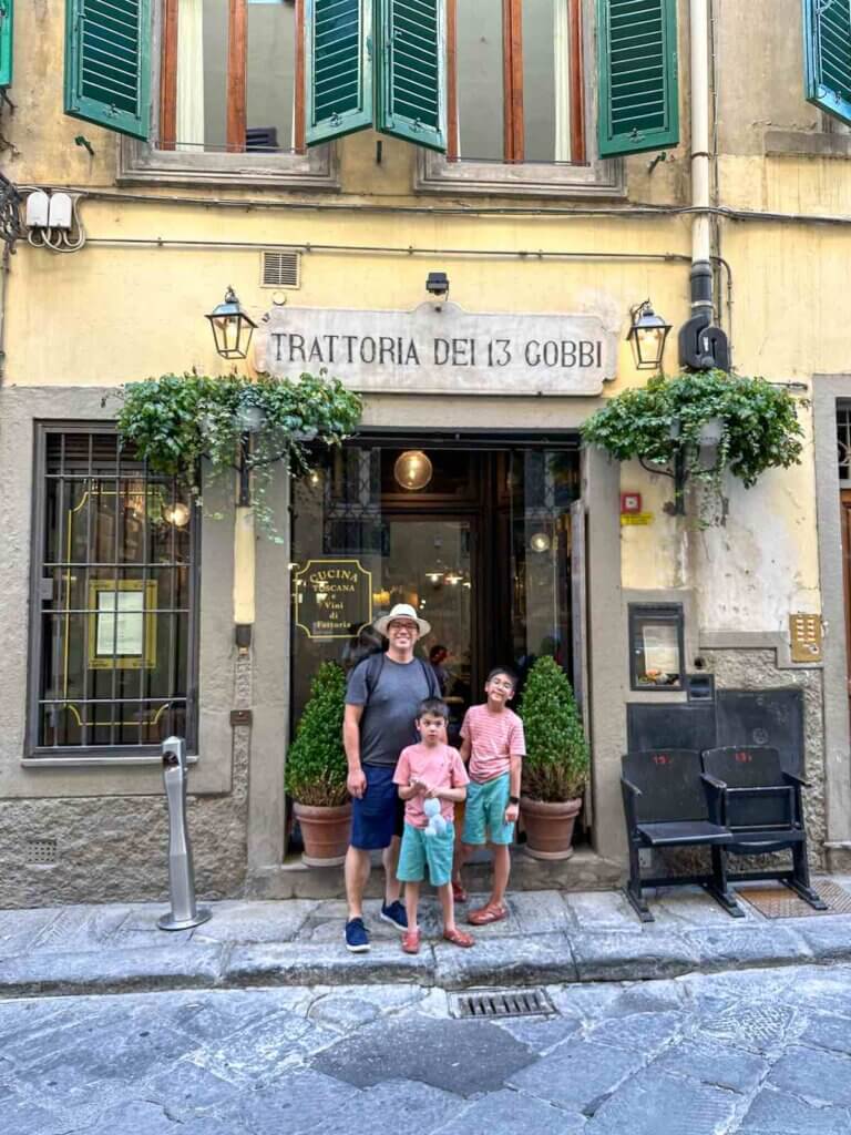 Image of a dad and two boys in front of Trattoria Dei 13 Gobbi restaurant in Florence Italy
