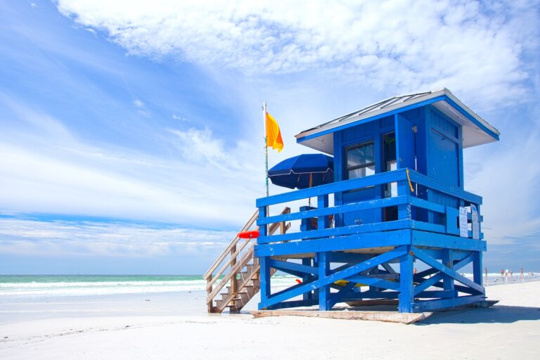 Check out the best US Family Vacation Ideas on a Budget recommended by top family travel blog Marcie in Mommyland. Image of Siesta Key Beach, Florida USA, colorful lifeguard house on a beautiful summer day with ocean and blue cloudy sky