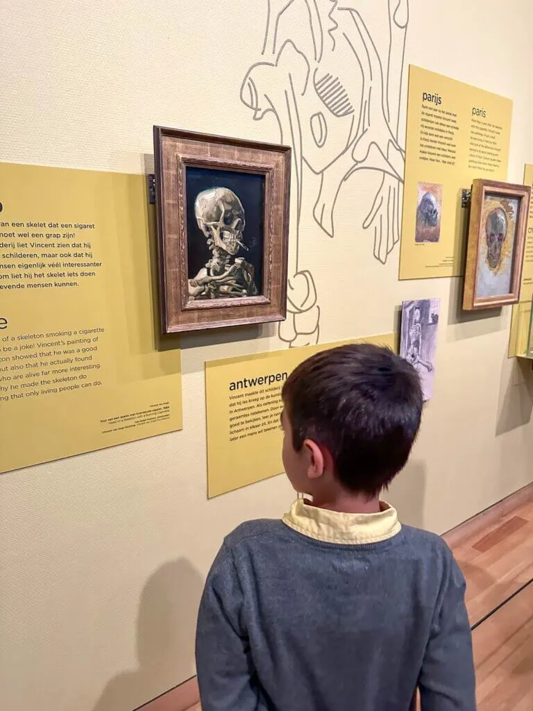 Image of a boy looking at a painting of a skeleton smoking a cigarette at the Van Gogh Museum in Amsterdam.
