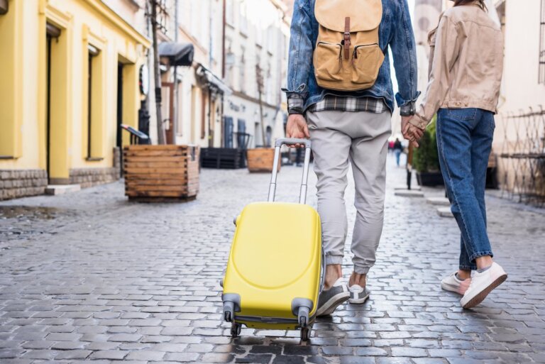 Find out helpful tips for traveling to Europe for the first time by top family travel blog Marcie in Mommyland. Image of a couple pulling a yellow suitcase down a cobblestone street in Europe
