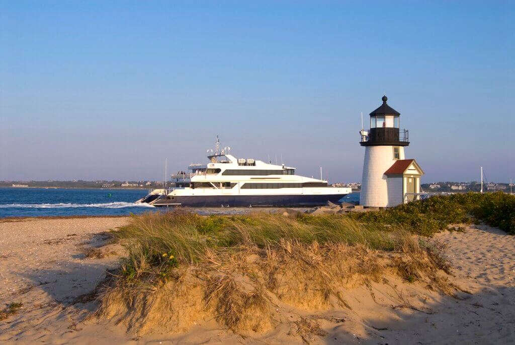 Ferry passes by Brant Point lighthouse at sunset on Nantucket Island, in Massachusetts.