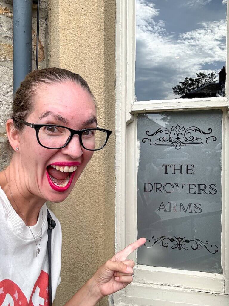 Image of a woman pointing at a window sign that says The Drover's Arms in Grassington, England in Yorkshire 
