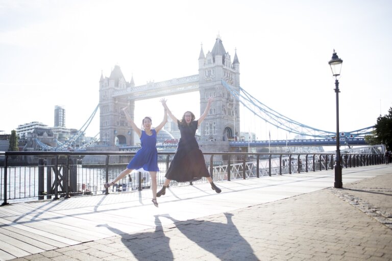 Find out what to do in London in a day with tips from top family travel blog Marcie in Mommyland. Image of two woman jumping in front of Tower Bridge