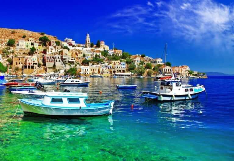 Find out how to plan a trip to Greece with tips from top family travel blog Marcie in Mommyland. Image of two boats in the water near a Greek island