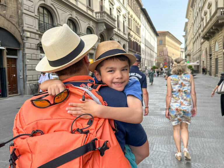 Find out if you should visit Italy or Spain for your next family vacation with tips by top family travel blog Marcie in Mommyland. Image of a dad carrying a boy on the streets of Italy. Photo credit: Marcie Cheung of Marcie in Mommyland