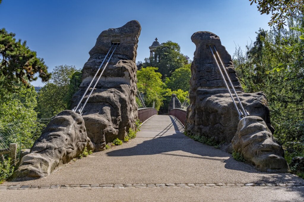 Park des Buttes Chaumont. View of the Footbridge joining the belvedere island, the Temple of the Sibyl and buildings behind