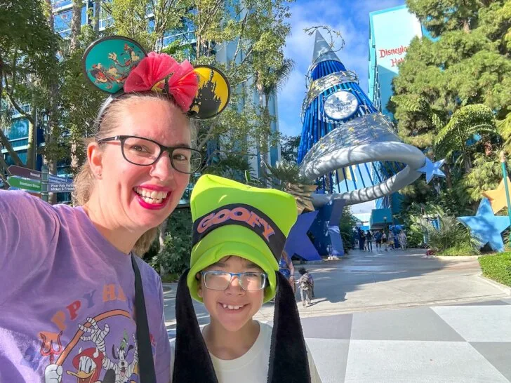 Check out this comparison of Universal Studios Hollywood vs Disneyland by top family travel blog Marcie in Mommyland. Image of Marcie Cheung and her son in front of the Disneyland Hotel