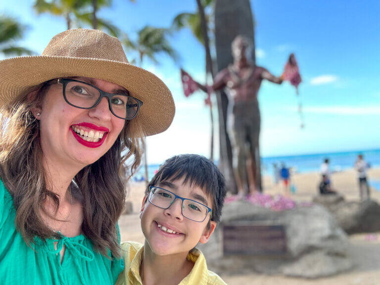 Check out the best Oahu resorts for families recommended by top family travel blog Marcie in Mommyland. Image of Marcie Cheung and her son in front of the Duke Kahanamoku statue in Waikiki.