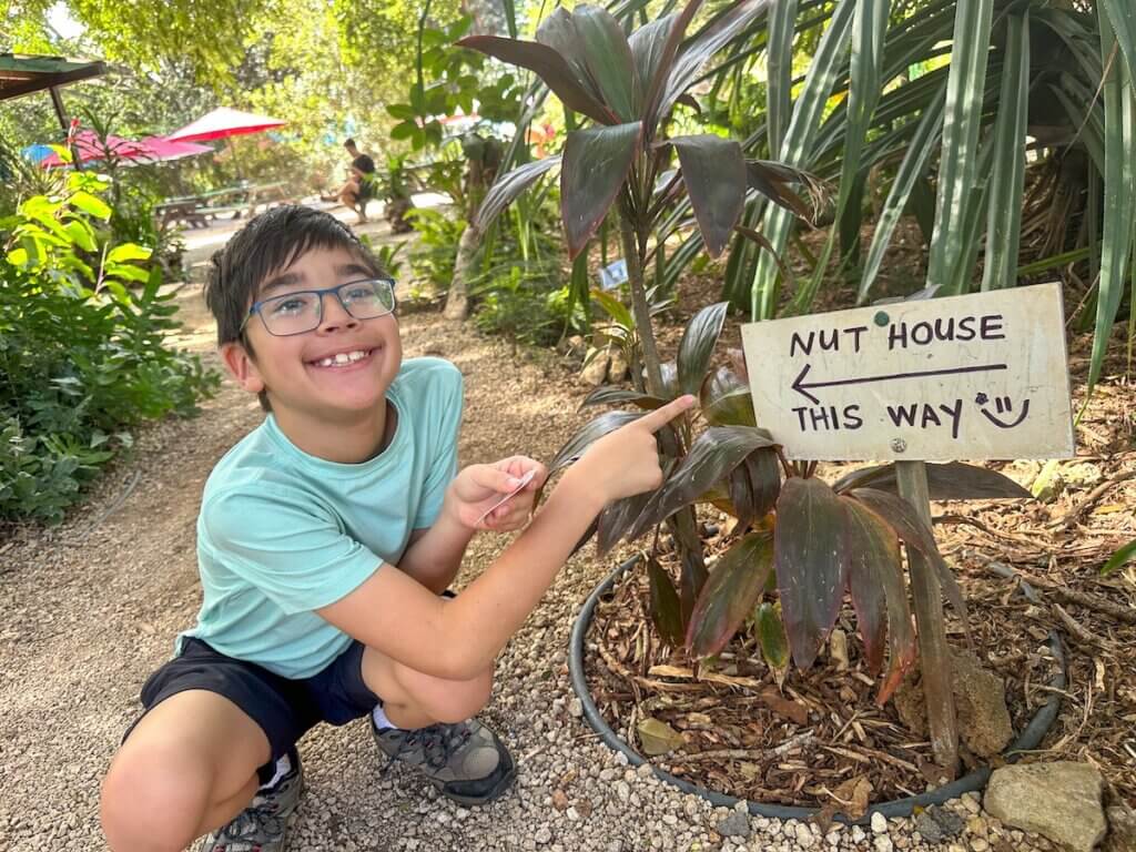 Image of a boy pointing at a sign that says Nut House This Way at a macadamia nut farm on Oahu. Photo credit: Marcie Cheung of Marcie in Mommyland