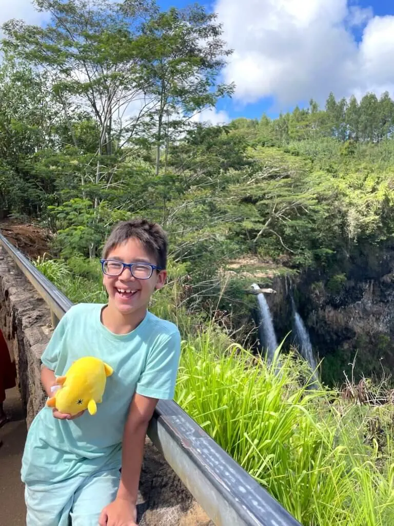 Image of a boy in front of Wailua Falls on Kauai. Photo credit: Marcie Cheung of Marcie in Mommyland